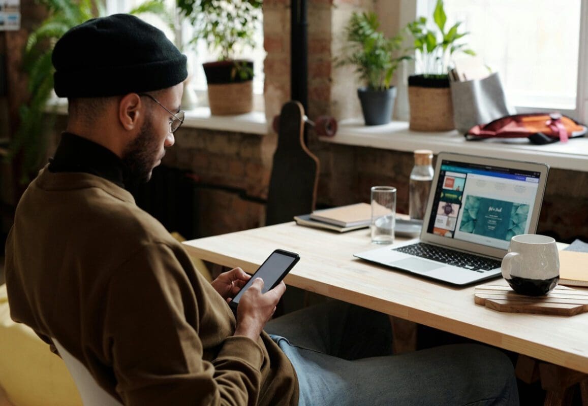 Man in ski hat looking at phone in front of computer desk