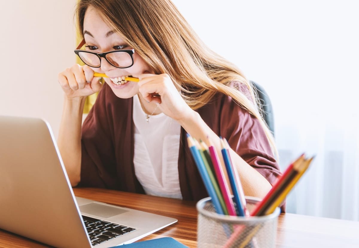 Woman looking at laptop frustrated bitin on a pencil